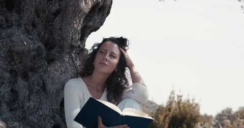 A woman is sitting under a tree and reading a book Stock Footage 284344085
