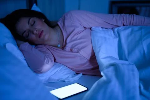 Woman sleeping in her bed while her smartphone is still on Stock Photos