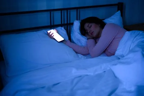 Woman sleeping in her bed while her smartphone is still on Stock Photos