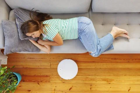 A woman sleeping on sofa while robot vacuum quietly takes care of the cleaning Foto stock