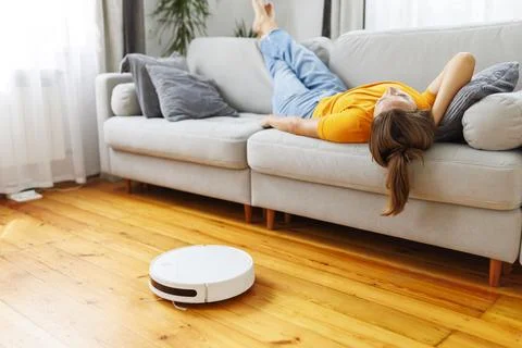 A woman sleeping on sofa while robot vacuum quietly takes care of the cleaning Stock Photos