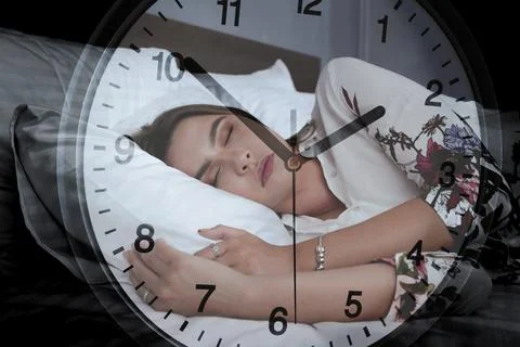 Woman sleeps on bed while clock shows time on a busy evening in a room Stock Photos