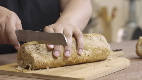 Woman slices bread using a knife on a wooden cutting board Stock Footage 135616945