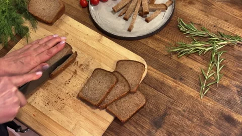 A woman slices rye gray bread on a wooden countertop in the kitchen 스톡 동영상 301240800