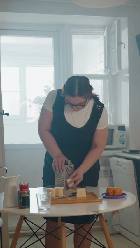 Woman slicing bread on round kitchen table under soft daylight backlight with Stock Footage 343678606