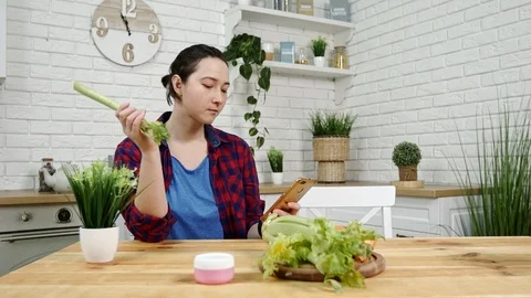 Woman with smartphone in hand eats celery at kitchen Video stock 101392266