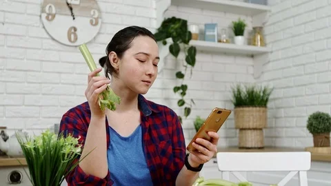 Woman with smartphone in hand eats celery at kitchen Stock-Footage 101395644