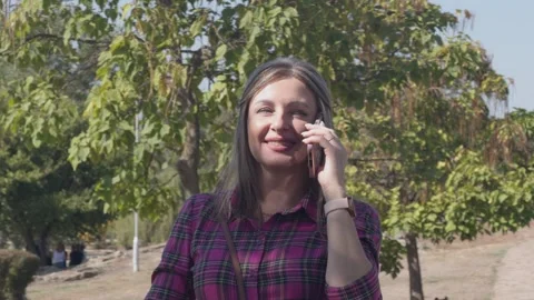A woman smiles while talking on a smartphone in a park Stock Footage 345832998