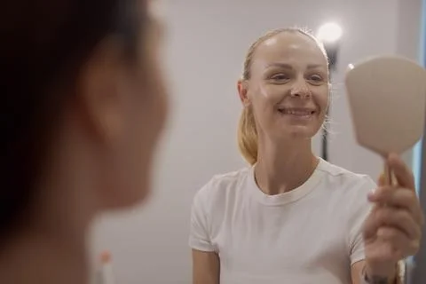 Woman smiling and looking at her reflection in a handheld mirror, experienc.. Stock Photos