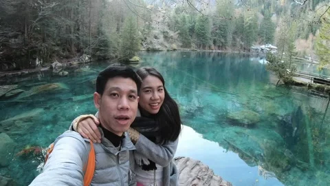 A woman is smiling and taking a selfie in front of a beautiful lake Stock Footage 322856450