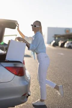 Woman smiling, loading paper shopping bags into a car trunk after shopping,.. Stock Photos