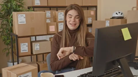 Woman smiling while checking smartwatch by stacked packages, courier labels.. Stock Footage 337358204