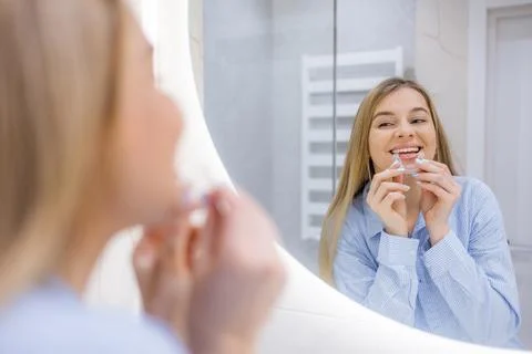 Woman smiling while fitting a transparent aligner in front of a bathroom mirr Stock Photos