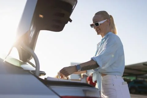 Woman smiling while loading multiple shopping bags into her car trunk after.. Stock Photos