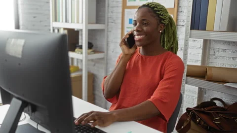 Woman smiling while talking on phone in modern office, computer on desk, vi.. 動画素材 296908662