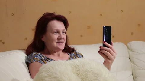 Woman smiling while talking via video call of her smartphone. She is sitting Video stock 145479721