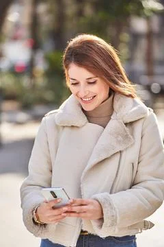 Woman smiling while using her mobile phone standing outdoors on the street. Foto stock