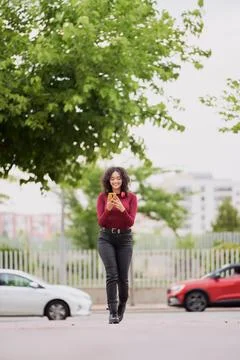 Woman smiling while using her mobile phone walking outdoors. 스톡 사진