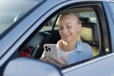 Woman smiling while using her smartphone inside a car, engaging with mobile.. Stock Photos