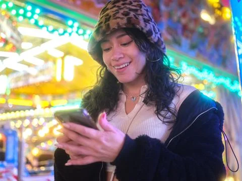 Woman smiling while using the mobile next to a fairground attraction Stock Photos