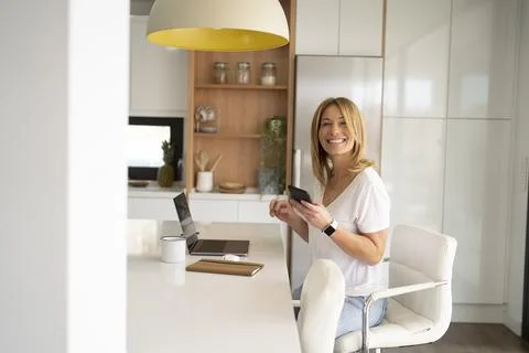 Woman Smiling While Using Phone at Kitchen Counter Stock Photos