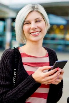 Woman Smiling While Using Smart Phone Outside Train Station Foto stock