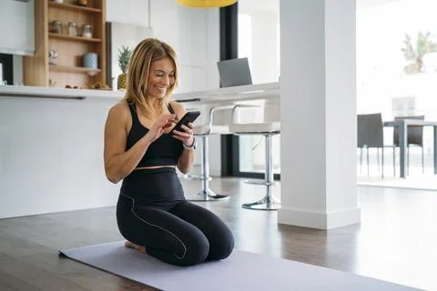 Woman Smiling While Using Smart phone on Yoga Mat Stock Photos