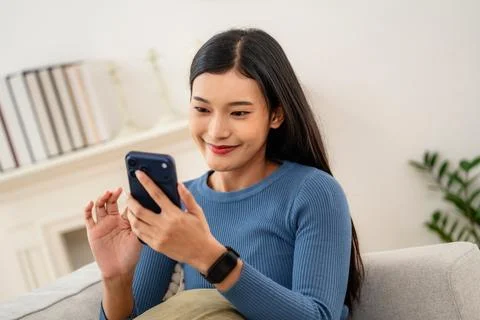 Woman smiling while using smartphone at home in a cozy living room during t.. Stock Photos