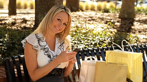 Woman smiling while working on mobile phone sitting with shopping bags Stock Footage 36473069