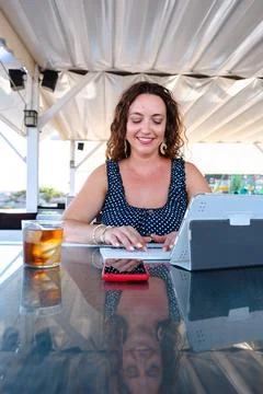 Woman smiling while working on tablet at outdoor cafe terrace with drink Foto stock
