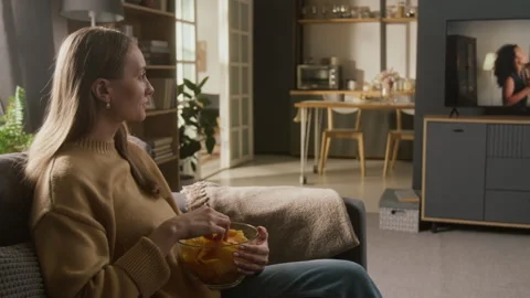 Woman Snacking on Chips while Attentively Watching Love Drama on TV Vídeos de archivo 331034149