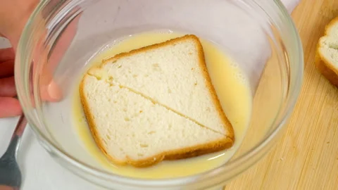 Woman soaking bread in whisked egg to fry toasts cooking on kitchen at home. Stock Footage 313132886