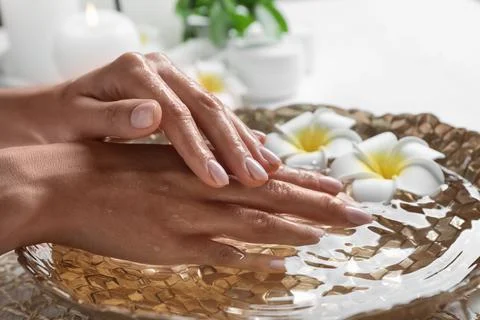 Woman soaking her hands in bowl of water and flowers on table, closeup with s Stock Photos