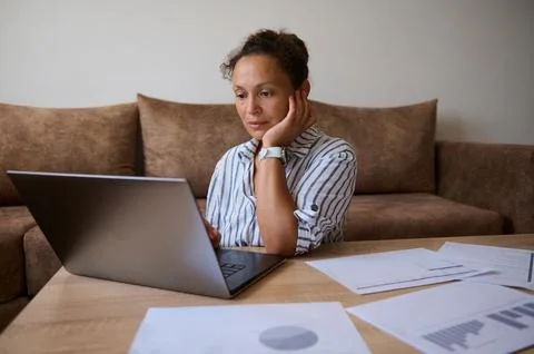 Woman at a sofa table using a laptop surrounded by charts and papers, working Foto stock