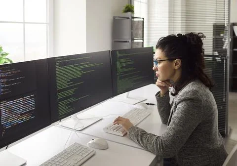 Woman software engineer coding at triple monitor setup in modern bright office 写真素材