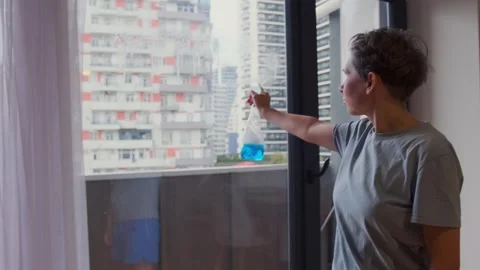Woman spraying cleaning solution on window glass using trigger bottle, preparing Stock Footage 333618536