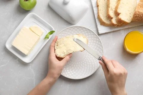 Woman spreading butter on slice of bread over table, closeup Stock Photos