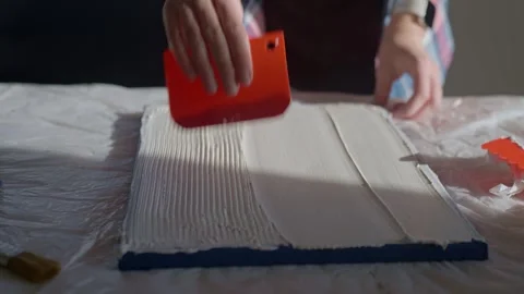 Woman spreading textured paste on white canvas using plastic scraper Video stock 331033528