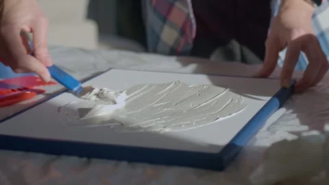 Woman spreading textured paste on white canvas using palette knife Video stock 331676578