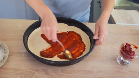 Woman spreading tomato paste on pizza dough at home kitchen Stock Footage 311812224