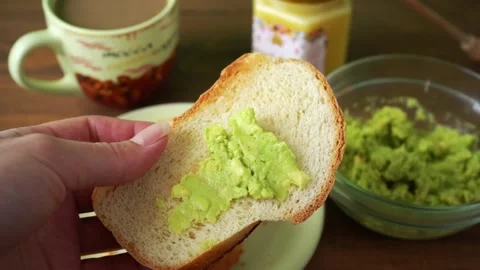 A woman spreads avocado pulp on toasted bread Stock Footage