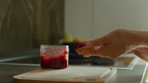 Woman spreads raspberry jam on slice of bread in modern kitchen setting Stock Footage 320952066
