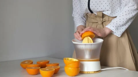 Woman is squeezing oranges using electric juicer in the kitchen, closeup view. Stock Footage 158197845