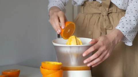 Woman is squeezing oranges using electric juicer in the kitchen, closeup view. Video stock 158917307