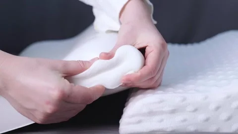 Woman squeezing a polyurethane pillow, demonstrating its memory foam ability to Stock Footage 299722182