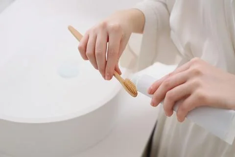 Woman squeezing toothpaste onto eco-friendly bamboo toothbrush for sustainabl Фото