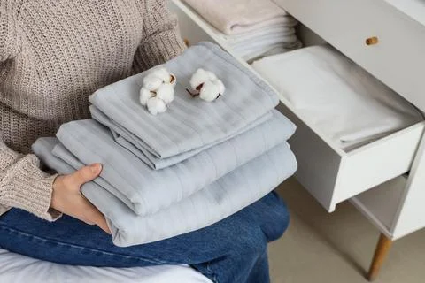 Woman with stack of bed sheets and cotton flowers at home Stock Photos