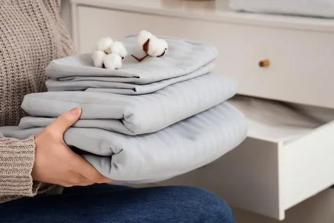 Woman with stack of bed sheets and cotton flowers at home Stock Photos