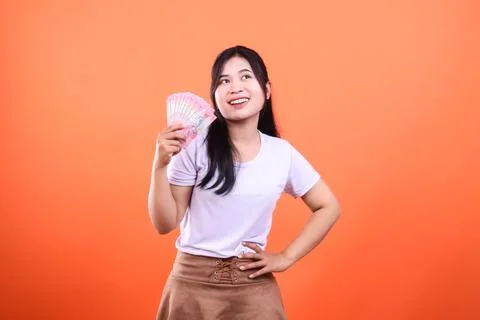 A woman with a stack of bills against a vibrant orange background smiles an.. Stock Photos