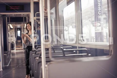 A Woman Standing Alone On A Bus Checking Her Cell Phone